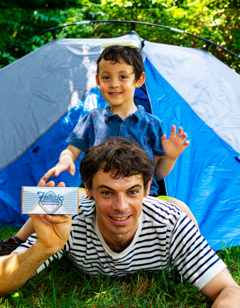 Max with waterproofer in front of a tent